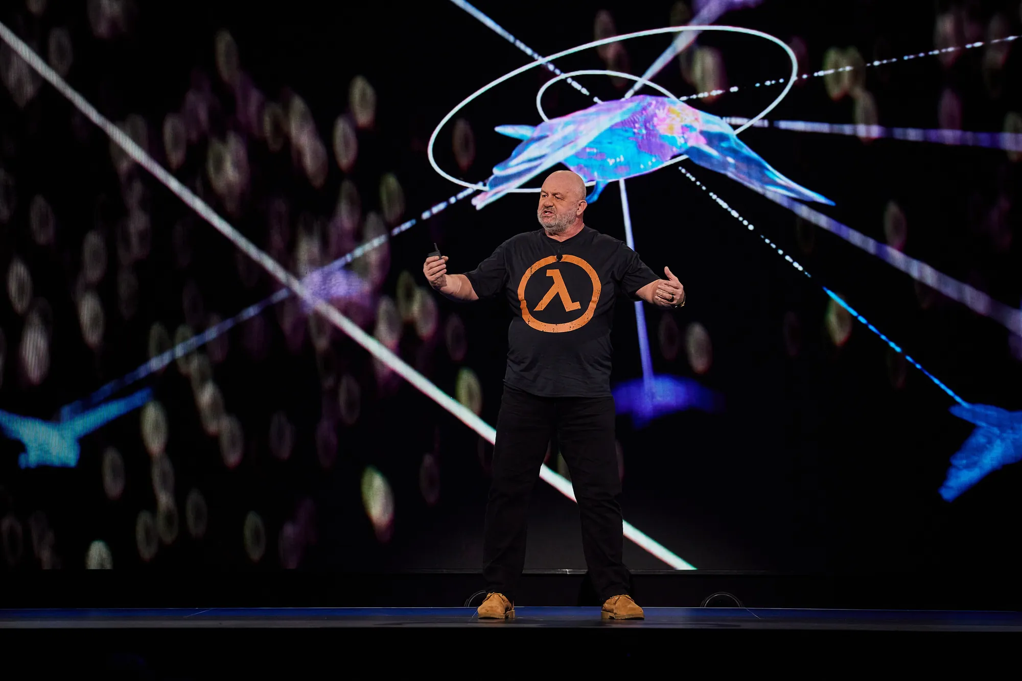 Werner Vogels on stage in a lambda t-shirt, lit by a projected galaxy