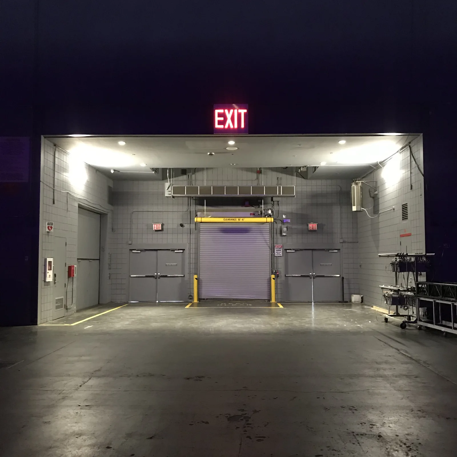 The loading bay behind the stage at the Javits Center, lit under a red exit sign.