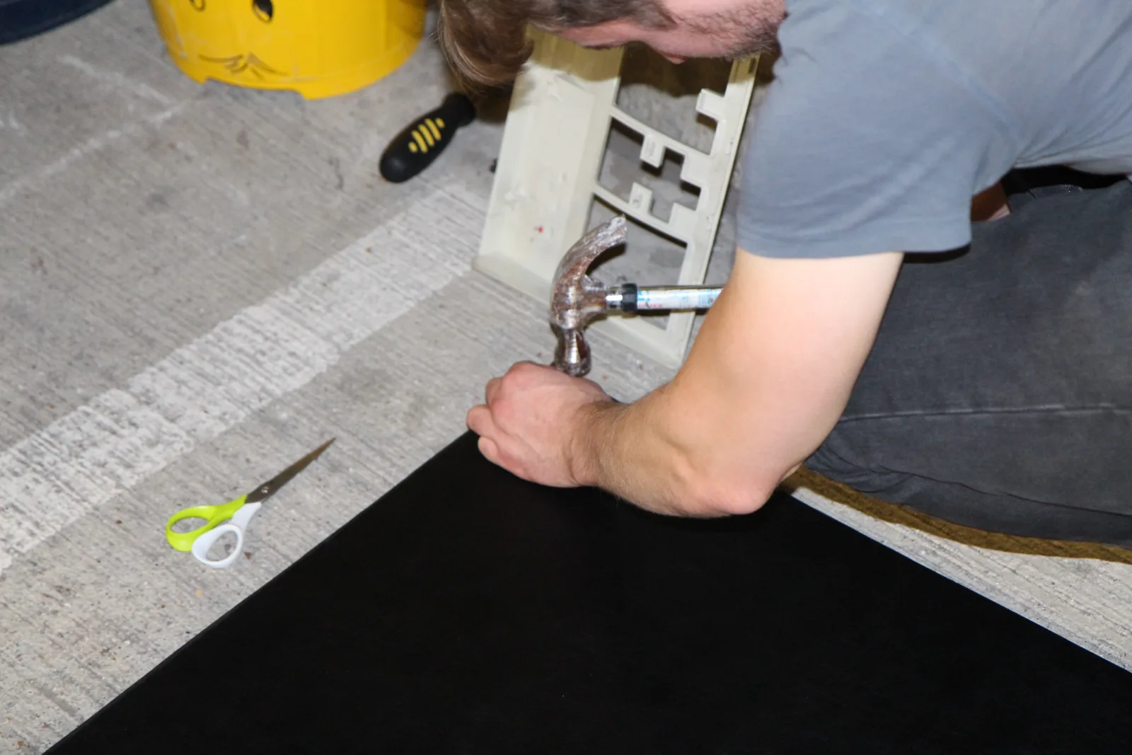 A builder hammering brass studs into black material stretched over a panel.
