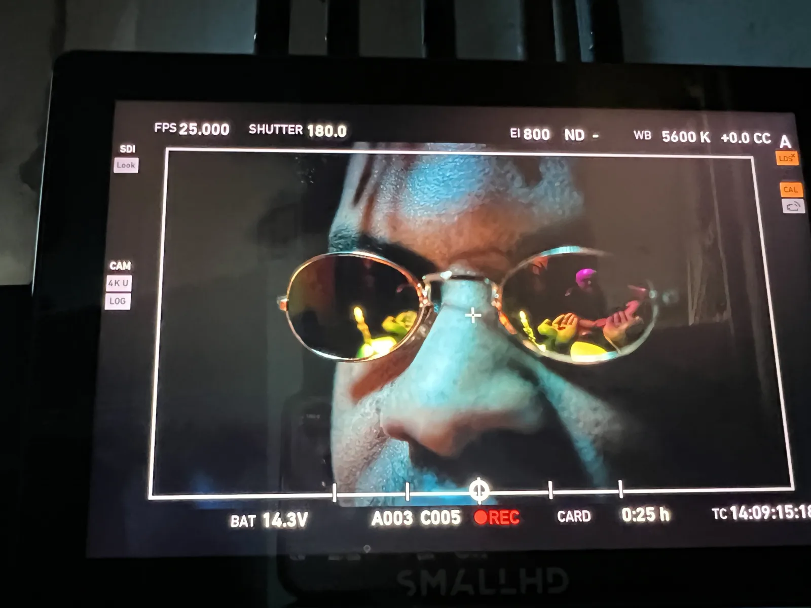 An extreme close-up on the monitor of Dr. Vogels in mirrored sunglasses, coloured light reflected in the lenses.