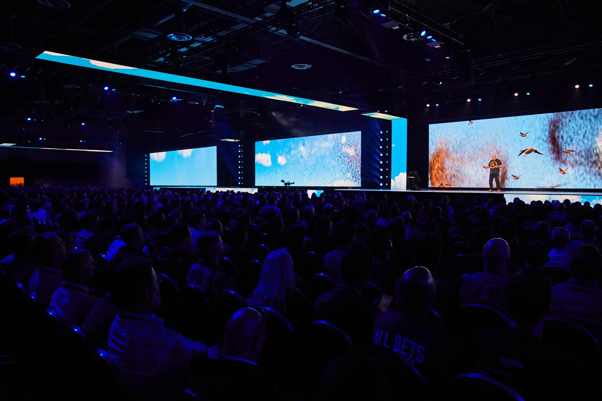 The keynote hall at re:Invent 2022, the audience in the dark facing three giant screens
