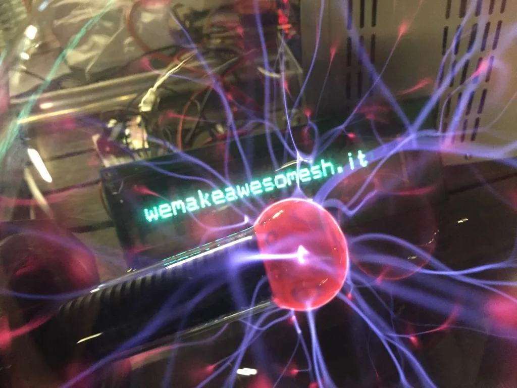 The plasma ball glowing inside the cabinet, beside a green display reading wemakeawesomesh.it.