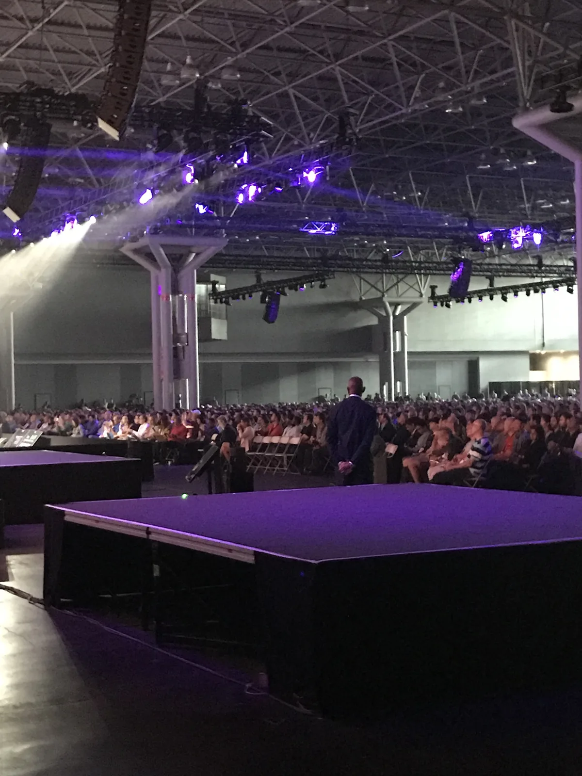 The view from the side of the stage across a packed keynote hall, lit purple.