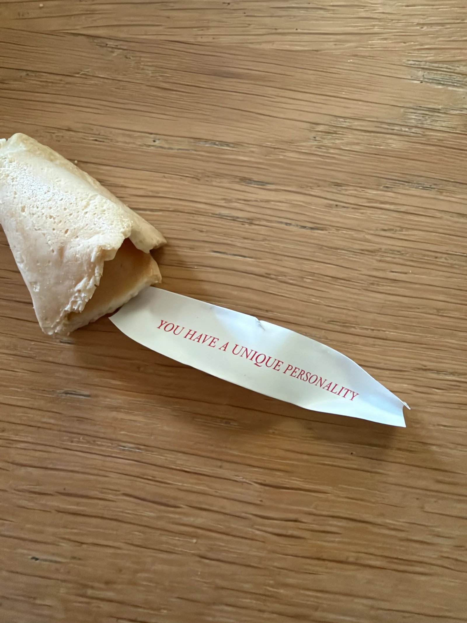 An open fortune cookie on a wooden table, its slip of paper reading "You have a unique personality".