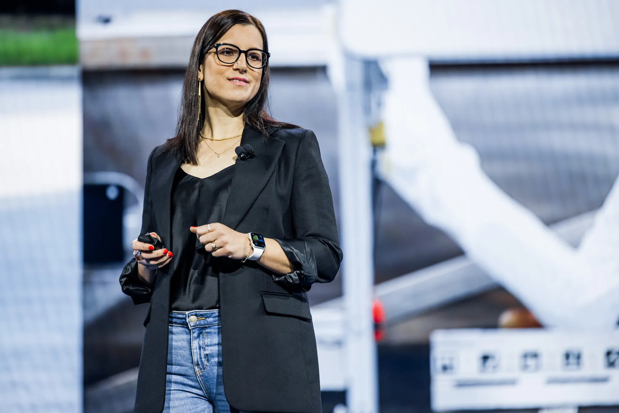 Roni Sole on stage, a robot arm on the screen behind her