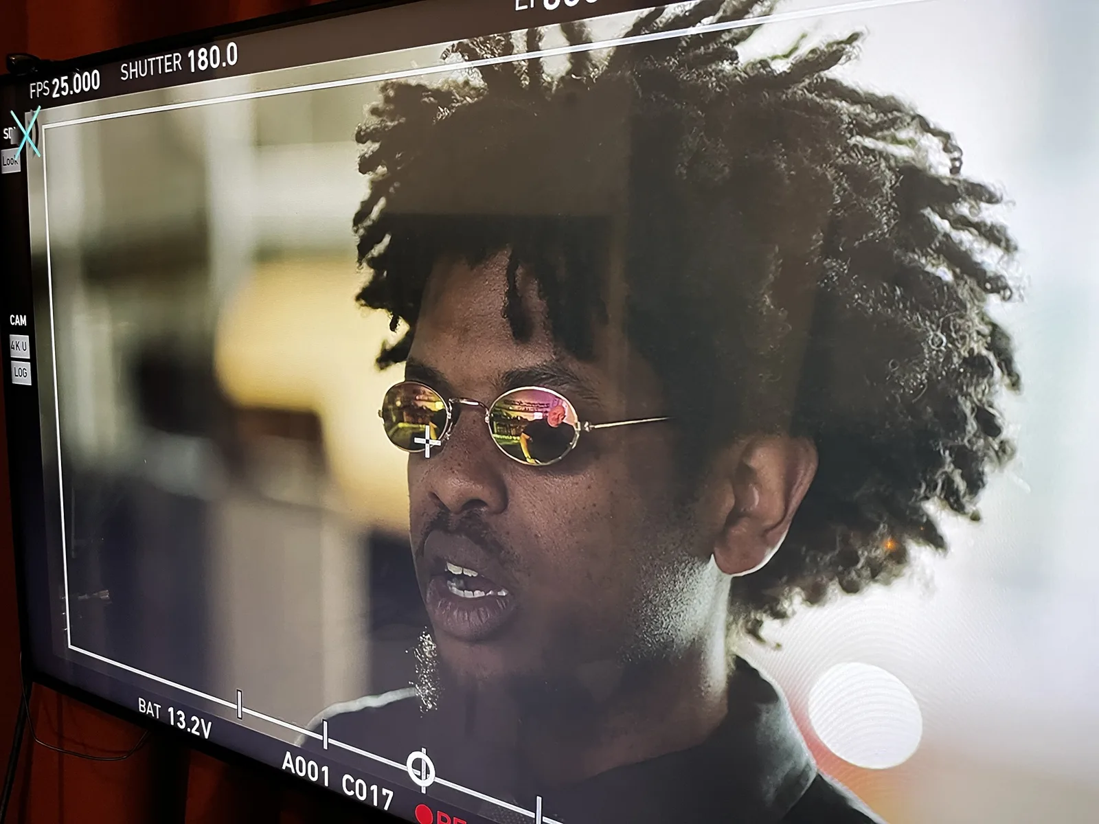 A close-up on the camera monitor of Terrance as Morpheus mid-line, the set reflected in his sunglasses.