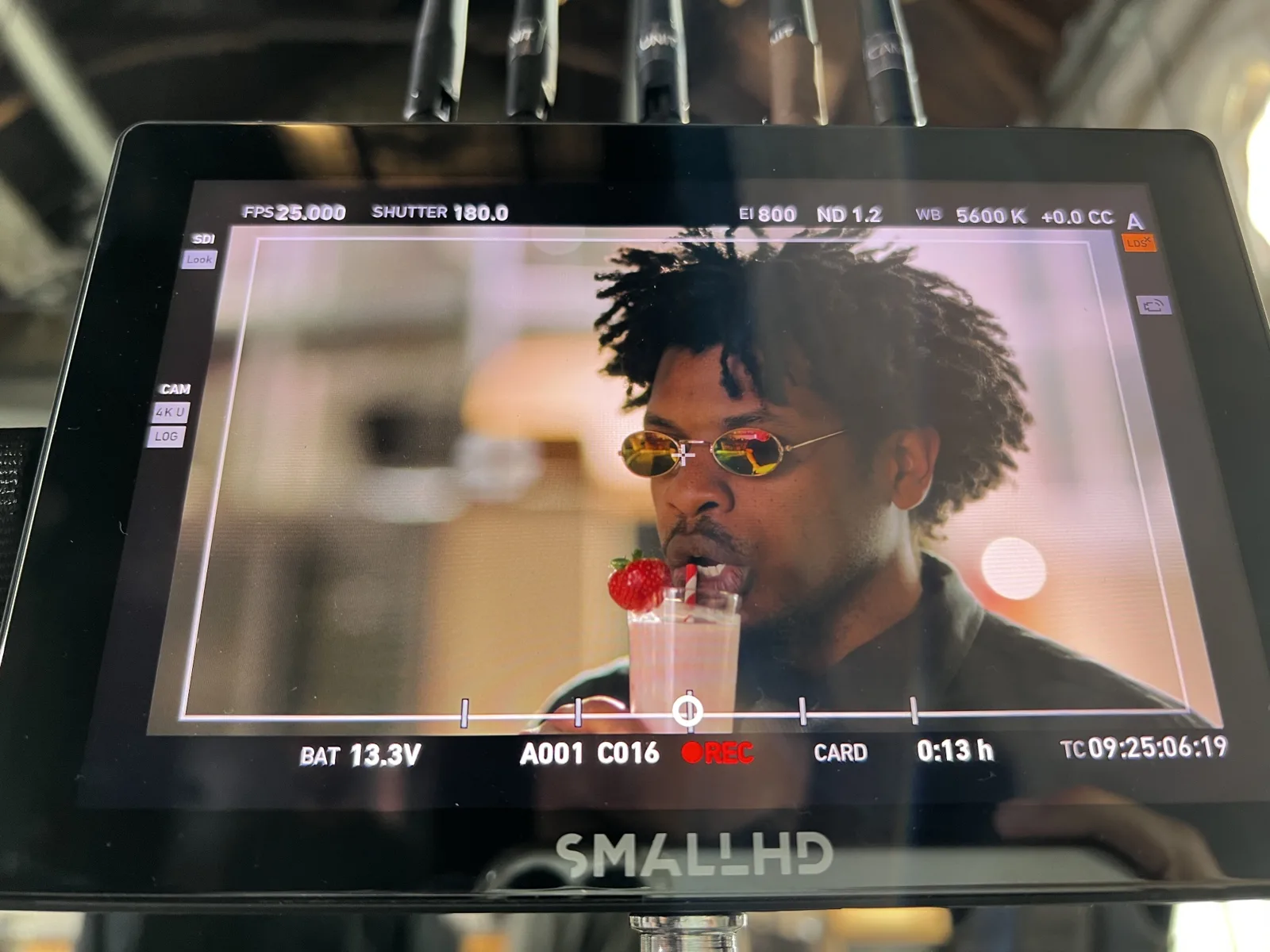 A camera monitor on set showing Terrance Lamonte Jr. as Morpheus, in round mirrored sunglasses, sipping a strawberry milkshake through a straw.