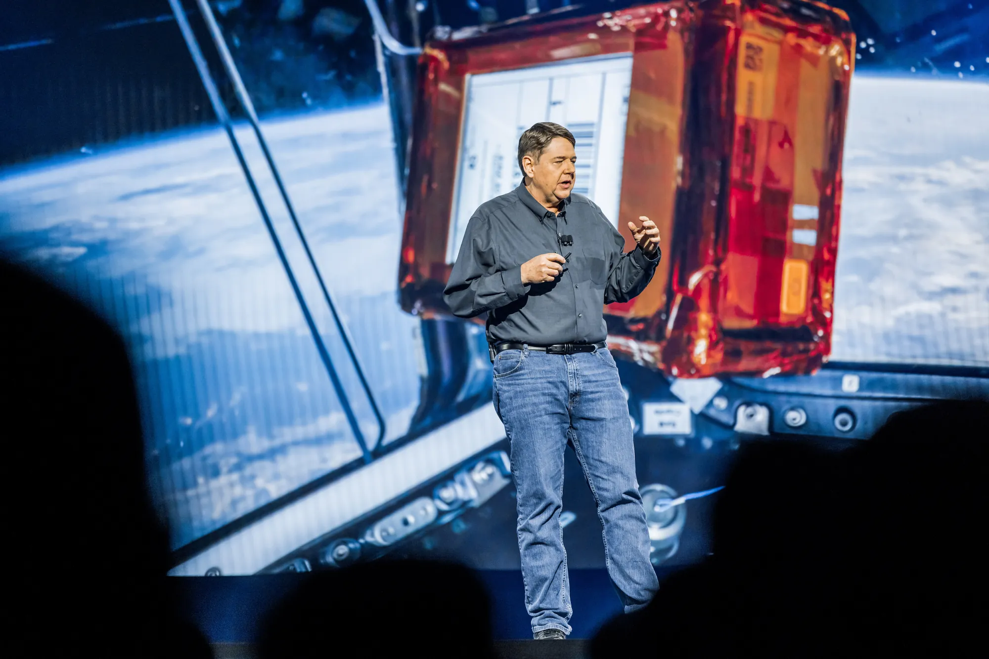 Bill Vass on stage, the parcel and the Earth on the screen behind