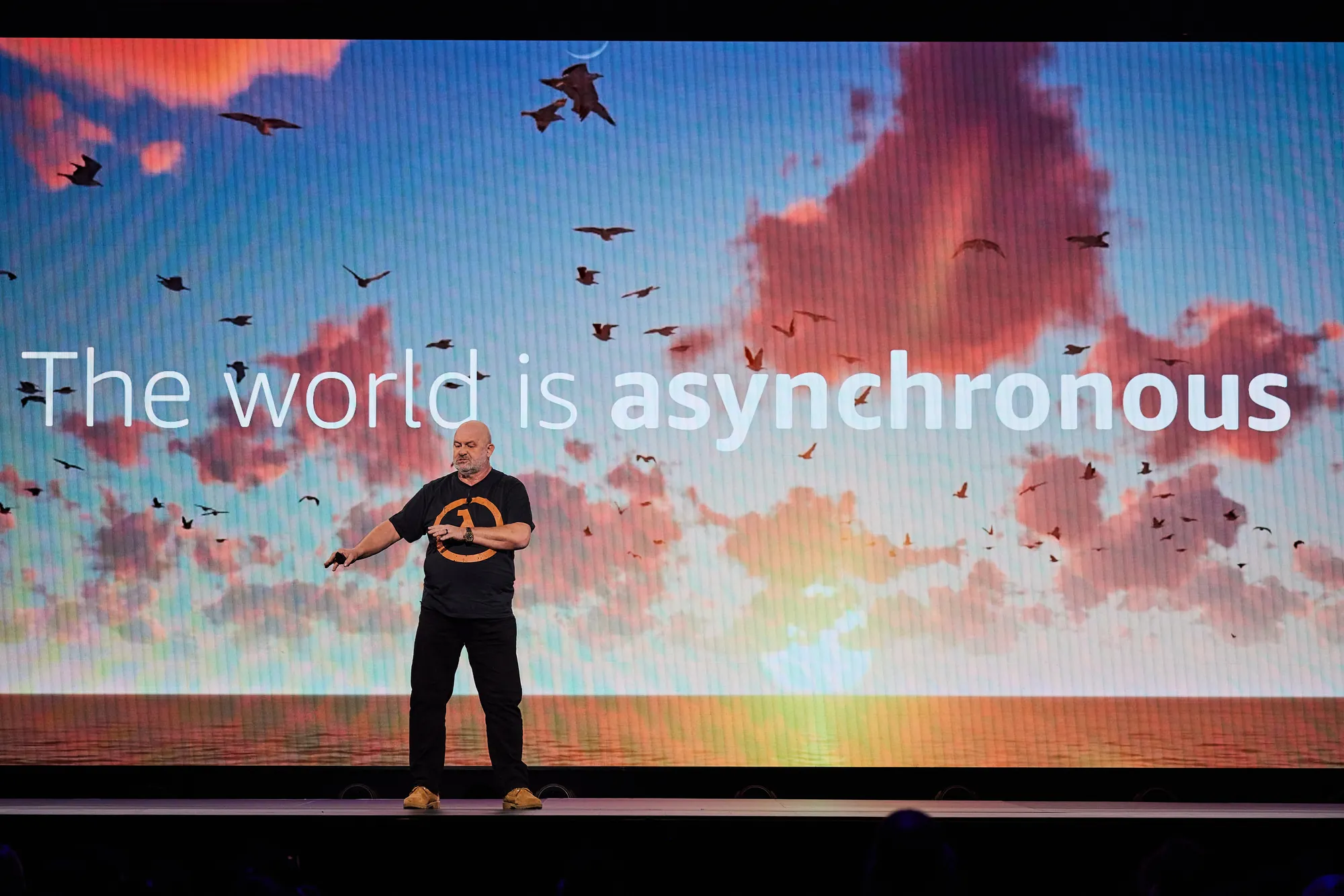 Werner Vogels in front of "The world is asynchronous", a sunset sky full of birds