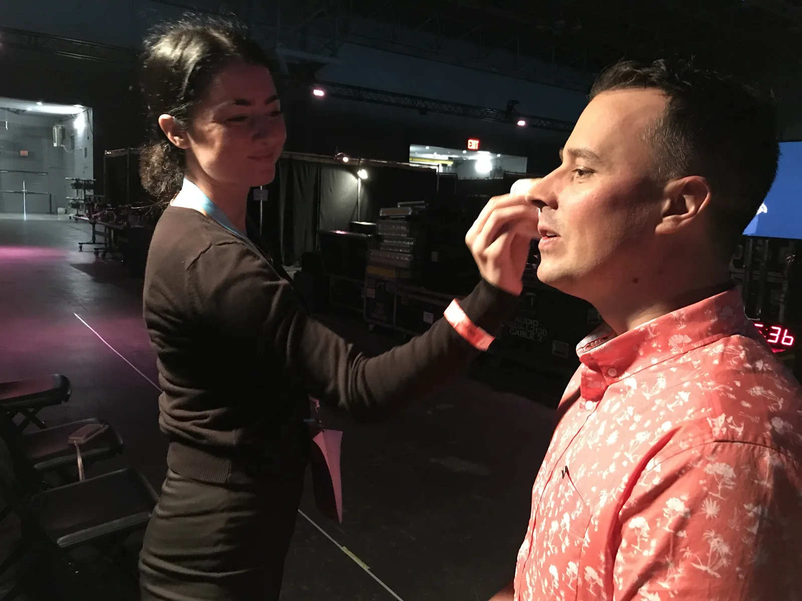 A make-up artist powdering Martin's face backstage, with flight cases and a countdown clock behind them.